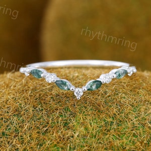 May include: A delicate silver ring with a v-shaped design. The ring is adorned with small, green marquise-shaped gemstones and a single, round diamond in the center.