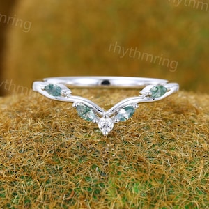 May include: A delicate silver ring with a V-shaped design featuring small green gemstones and a single diamond in the centre.