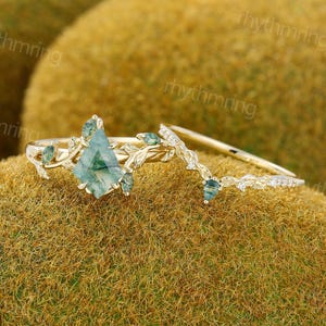 May include: A gold ring set. The main ring has a large, light green, diamond-shaped stone and smaller green stones. The band has a leaf design. The second ring is a curved band with small white stones and a green stone.