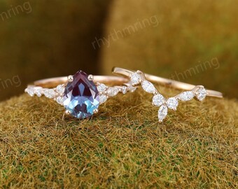 May include: A pear-shaped alexandrite engagement ring set in rose gold with a delicate diamond band and a matching diamond v-shaped wedding band.