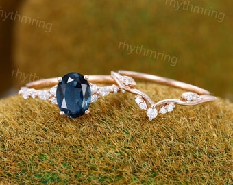 Può includere: Un set di due anelli in oro rosa con una pietra preziosa ovale blu e piccoli diamanti. L'anello di fidanzamento presenta una pietra preziosa ovale blu più grande circondata da piccoli diamanti. La fascia nuziale è una fascia delicata e curva con piccoli diamanti.