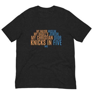 Op de afbeelding: Een donker antracietgrijs T-shirt met korte mouwen en tekst in oranje en lichtblauw. De tekst luidt: MY MAYOR MUSLIM, MY BAGEL'S JEWISH, MY CHRISTIAN DIOR, KNICKS IN FIVE en NYC. Het T-shirt heeft een ronde hals en een standaard pasvorm.