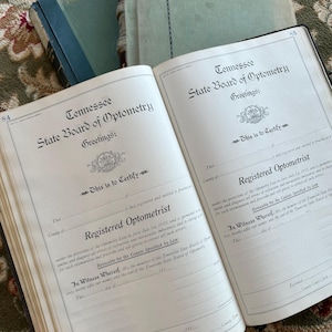 May include: An open book displaying two identical pages titled Tennessee State Board of Optometry. The text reads This is to Certify that is duly registered and entitled to practice as a Registered Optometrist under the provisions of the Optometry Law.
