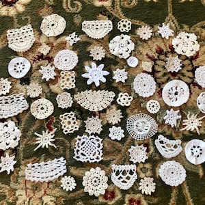May include: A collection of white crocheted doilies of various shapes and sizes, arranged on a green and brown patterned carpet.