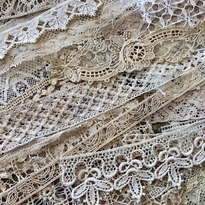 May include: A collection of assorted lace trims in various shades of cream, beige, and off-white. The strips feature diverse intricate patterns including floral motifs, geometric mesh, scalloped edges, and delicate needlework designs layered together.