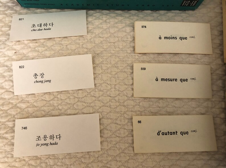 以下が含まれることがあります： 韓国語とフランス語の単語とフレーズが書かれたフラッシュカードのセット。カードは白地に黒文字。韓国語の単語はハングル、韓国のアルファベットで書かれています。フランス語の単語はラテン文字で書かれています。カードは821、822、746、574、559、66と番号が付けられています。