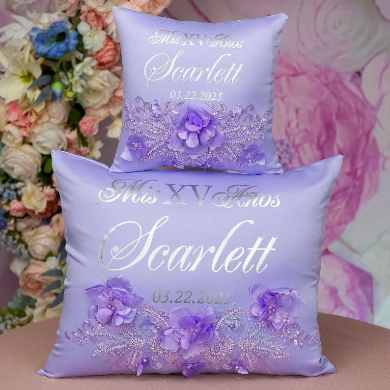 May include: Two lavender satin pillow covers with silver embroidery. The top pillow cover has the text "Mis XV Anos Scarlett 03.22.2025" and the bottom pillow cover has the text "Mis XV Anos Scarlett 03.22.2023".