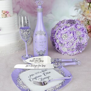 May include: Purple and silver Quincea&ntilde;era party decorations including a bottle of sparkling wine, a cake knife and server, a champagne flute, and a bouquet of flowers.