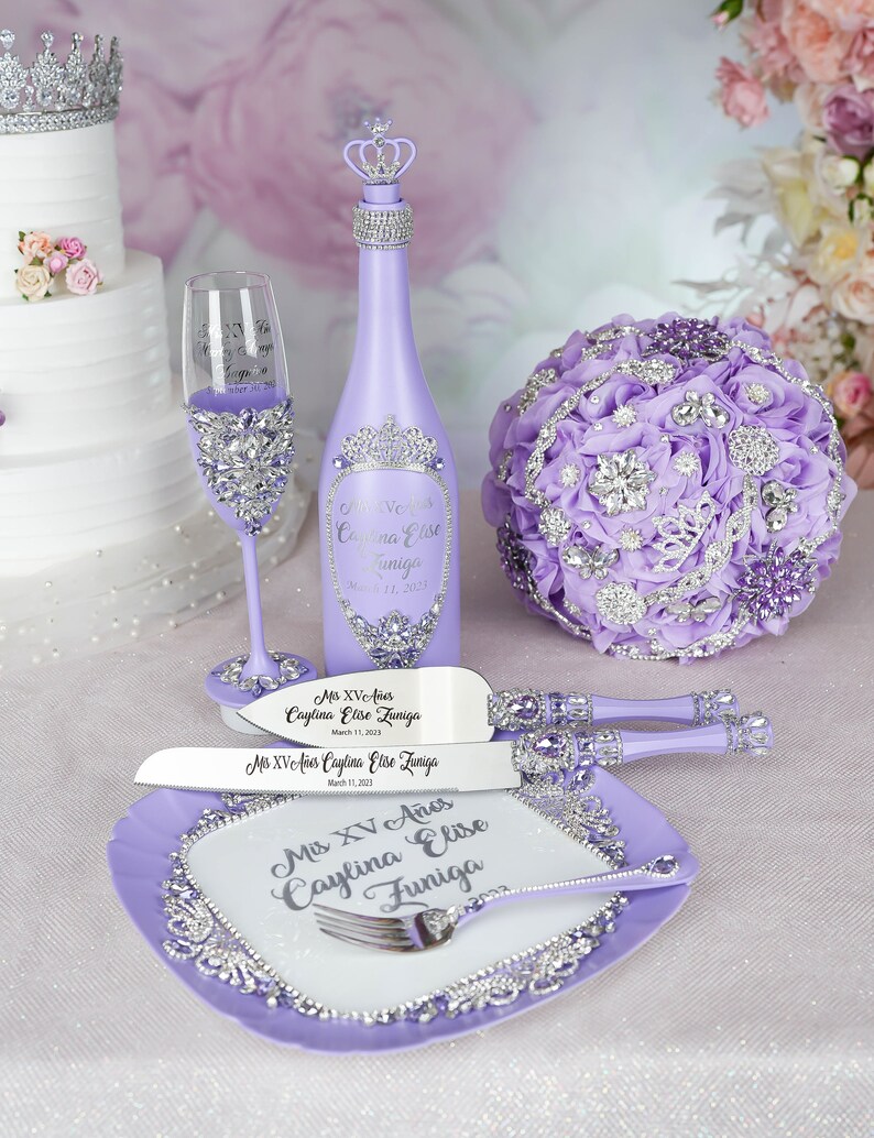May include: Purple and silver Quincea&ntilde;era party decorations including a bottle of sparkling wine, a cake knife and server, a champagne flute, and a bouquet of flowers.