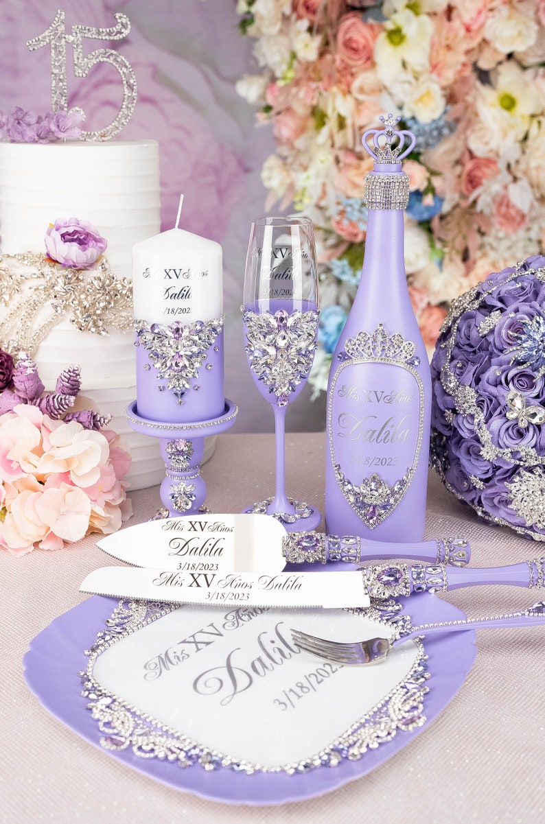 May include: Purple and silver Quincea&ntilde;era party decorations including a cake knife and server, a bottle of sparkling wine, a candle, a champagne flute, and a decorative plate. The decorations are personalized with the name "Dalila" and the date "3/18/2023".