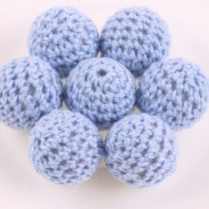 May include: A set of seven light blue crocheted wooden beads. The beads are round and have a delicate crocheted pattern.