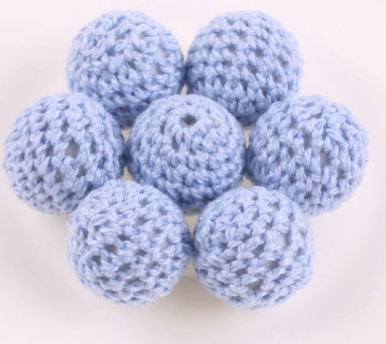 May include: A set of seven light blue crocheted wooden beads. The beads are round and have a delicate crocheted pattern.