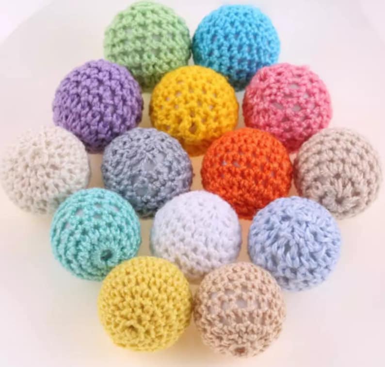 May include: A collection of 12 crocheted wooden beads in various colors, including light blue, pink, yellow, green, white, and gray. The beads are all the same size and have a textured surface.