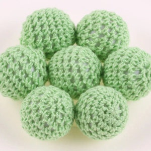 May include: Seven green crocheted balls with a white center. The balls are arranged in a circle with the white centers facing outward.