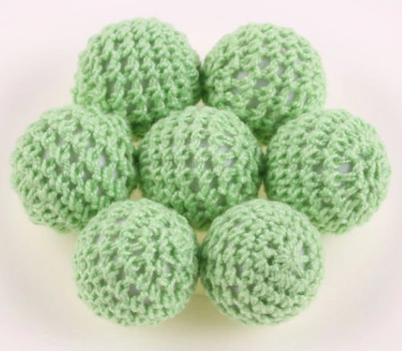 May include: Seven green crocheted balls with a white center. The balls are arranged in a circle with the white centers facing outward.