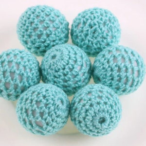 May include: A group of seven crocheted balls in a light blue color. The balls are arranged in a circle, with the center ball slightly raised.