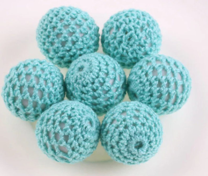 May include: A group of seven crocheted balls in a light blue color. The balls are arranged in a circle, with the center ball slightly raised.