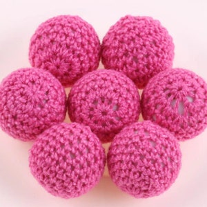 May include: Seven pink crocheted balls, each with a delicate, intricate pattern. The balls are arranged in a circle, with the center of the circle slightly raised.
