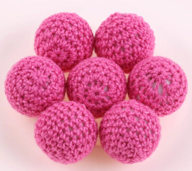 May include: Seven pink crocheted balls, each with a delicate, intricate pattern. The balls are arranged in a circle, with the center of the circle slightly raised.