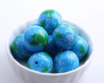 May include: A white bowl filled with blue and green globe-shaped beads. The beads have a marbled effect with white, blue, and green swirls.