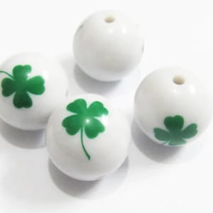 May include: Four white ceramic beads with green four-leaf clover designs.