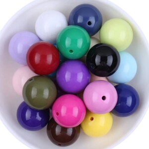 May include: A collection of 18 colorful round plastic beads in various colors, including purple, pink, red, green, blue, yellow, brown, and white.
