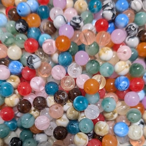 May include: A collection of colorful, round beads in various sizes and shades. The beads are a mix of translucent and opaque, with colors including blue, pink, orange, green, and brown. Some beads have a marbled effect.