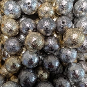 May include: A collection of spherical beads featuring a textured, metallic foil finish in alternating shades of silver and gold. Each bead has a small, centered hole visible on its surface, creating a reflective and crinkled appearance throughout.
