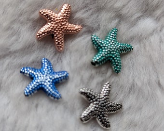 May include: Four starfish charms in different colors: rose gold, teal, silver, and blue. The charms are made of metal and have a textured surface.