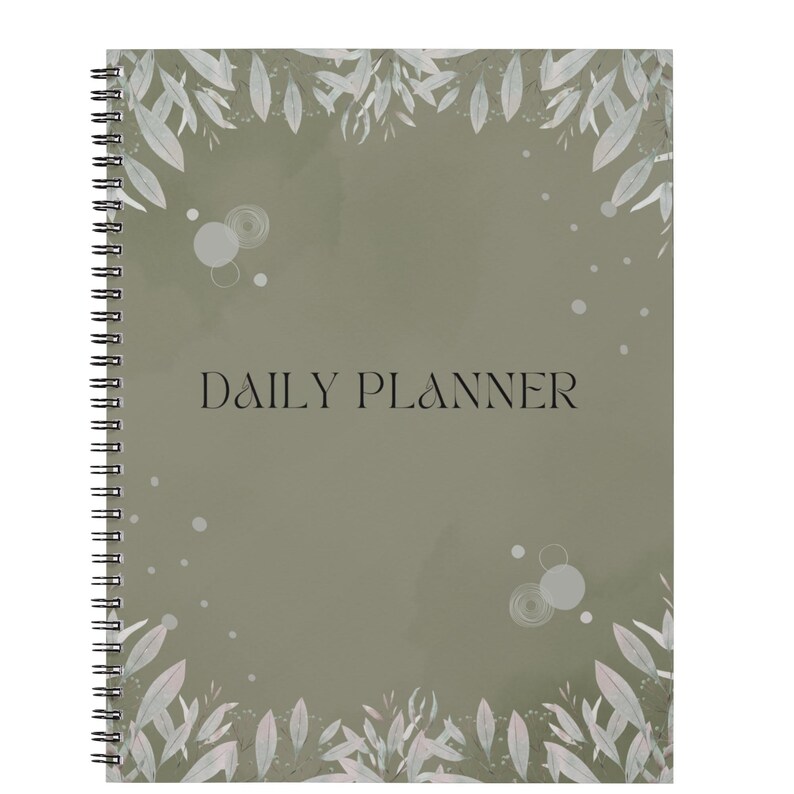 May include: A spiral-bound daily planner with a sage green cover featuring a botanical leaf border at the top and bottom. The text DAILY PLANNER is printed in black in the centre, surrounded by small white circular accents and soft leaf illustrations.