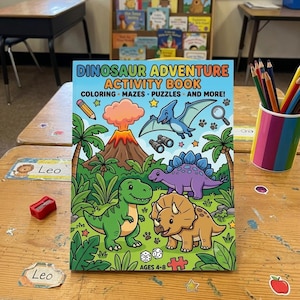 May include: A colorful "Dinosaur Adventure Activity Book" with illustrations of dinosaurs, a volcano, and palm trees. The book cover features the text "COLORING MAZES PUZZLES AND MORE!" and is designed for ages 4-8. The book is on a wooden desk.