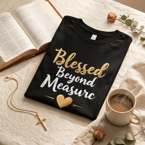 May include: A black t-shirt featuring the gold and white text Blessed Beyond Measure with a gold heart icon. The shirt is displayed alongside an open book, a gold cross necklace, a ceramic mug of coffee, and dried floral stems.