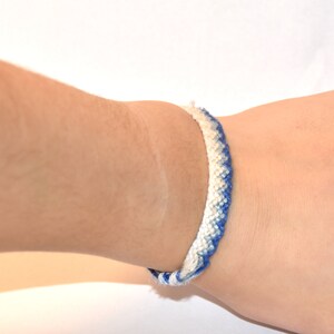 May include: A blue and white friendship bracelet with a chevron pattern.