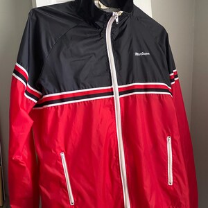 May include: A red and black windbreaker jacket with white stripes and a white zipper. The jacket has a white logo that says "MacGregor" on the left chest.