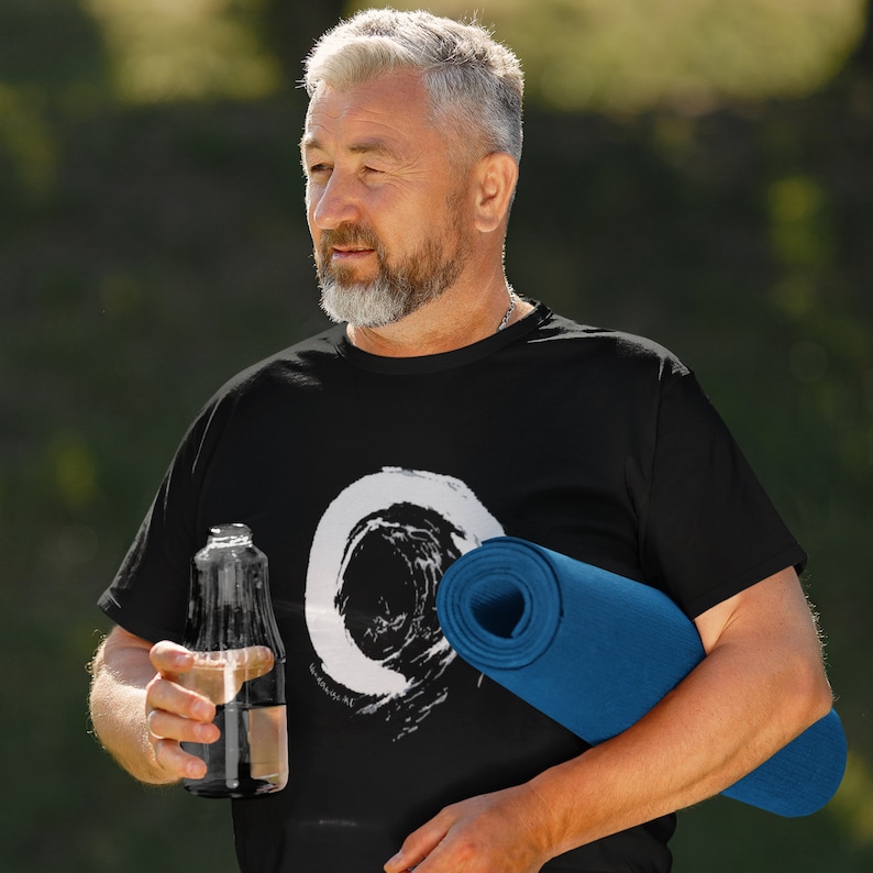 May include: Black t-shirt with a white wave design and a blue yoga mat. A clear glass bottle with water is held in the hand. The image is taken outdoors.
