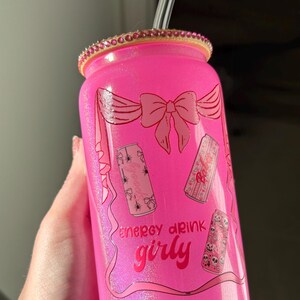 May include: Pink glittery glass can with a clear straw and a bedazzled rim. The can features a bow design and the words "energy drink girly" with illustrations of cans with spooky designs.