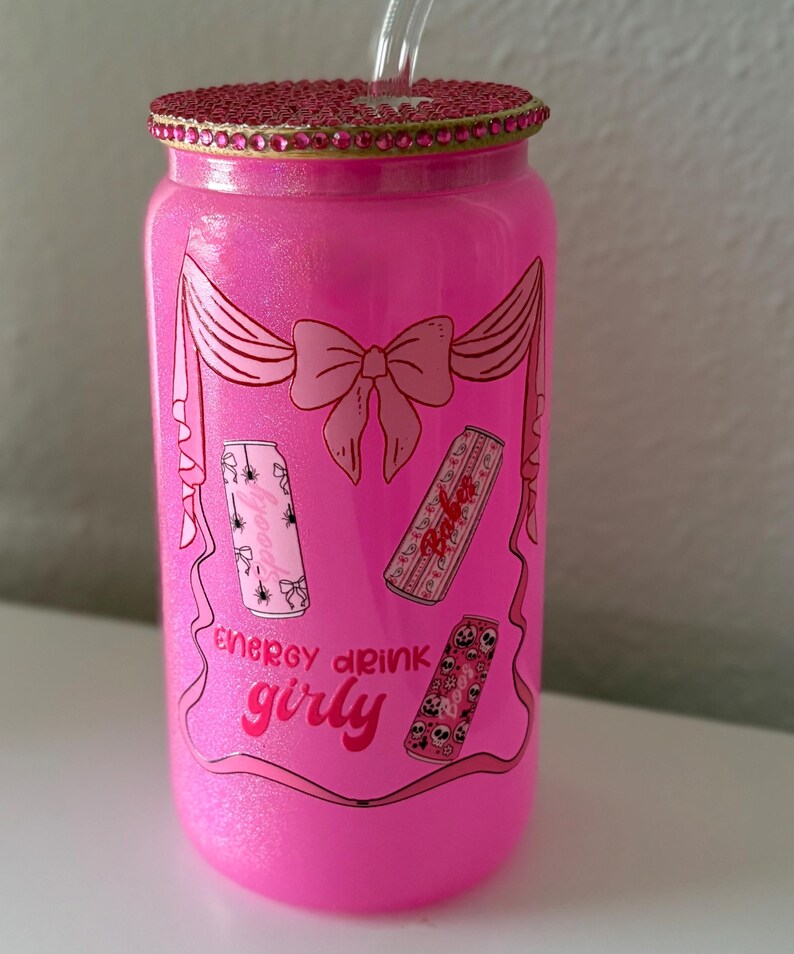 May include: A pink glittery glass can-shaped tumbler with a decorative lid and straw. The tumbler features a bow design and the words "energy drink girly" with illustrations of energy drink cans.
