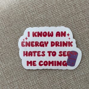 May include: White sticker with red text that reads "I know an energy drink hates to see me coming". A purple and white can is pictured next to the text.