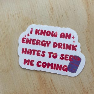 May include: White sticker with pink text that reads "I know an energy drink hates to see me coming". A purple and white energy drink can is in the bottom right corner of the sticker.