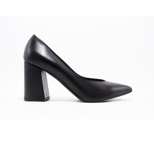 以下が含まれることがあります： 黒革のポインテッドトゥパンプスで、太いブロックヒールが付いている
