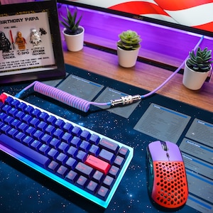 Peut inclure: Un bureau avec un clavier personnalisé, une souris et un cadre avec un thème Star Wars. Le clavier a un rétroéclairage bleu et violet et la souris est rouge et noire. Le tapis de bureau a un imprimé galaxie.