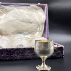 Puede incluir: Un juego de vasos de chupito de plata con un diseño grabado, en una caja forrada de terciopelo morado.