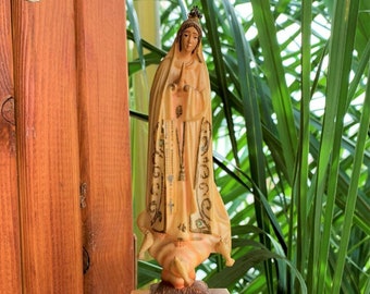 Può includere: Una piccola scatola di legno con una statuetta della Vergine Maria in cima. La scatola è dipinta di marrone e ha la scritta "FATIMA" sul davanti.