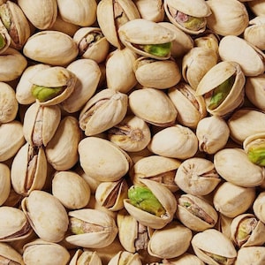 Puede incluir: Una imagen de primer plano de un montón de pistachos. Las nueces son de color beige claro y algunas están abiertas, revelando los granos verdes en el interior.