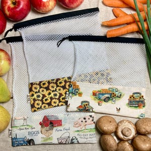Könnte beinhalten: Wiederverwendbare Gemüsebeutel aus Netzstoff mit dekorativen Stoffböden. Eine Tasche zeigt Sonnenblumen, eine andere einen Oldtimer-Truck mit Sonnenblumen und die dritte eine Farm-Szene mit dem Text "Eggs for Sale". Äpfel, Birnen, Karotten und Pilze sind ebenfalls sichtbar.