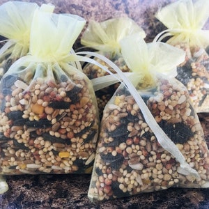 May include: Four small yellow organza bags filled with a variety of birdseed. The bags are tied with white ribbon.