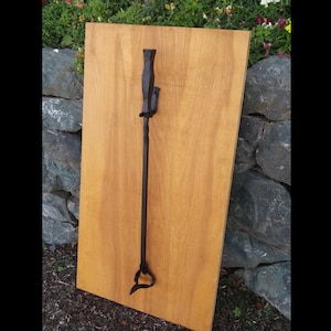 May include: Black metal fireplace tool with a twisted handle and a hook at the top. The tool is mounted on a wooden wall.