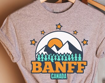 May include: Gray t-shirt with a graphic of mountains, a sun, and trees. The text "BANFF CANADA" is printed below the graphic.