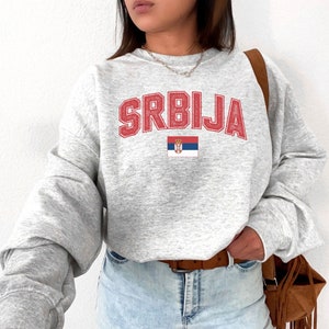 May include: Gray sweatshirt with the word "SRBIJA" in red letters and the Serbian flag printed on the front.