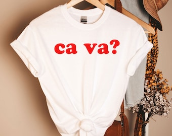 Op de afbeelding: Wit T-shirt met de tekst "ca va?" in rode letters.